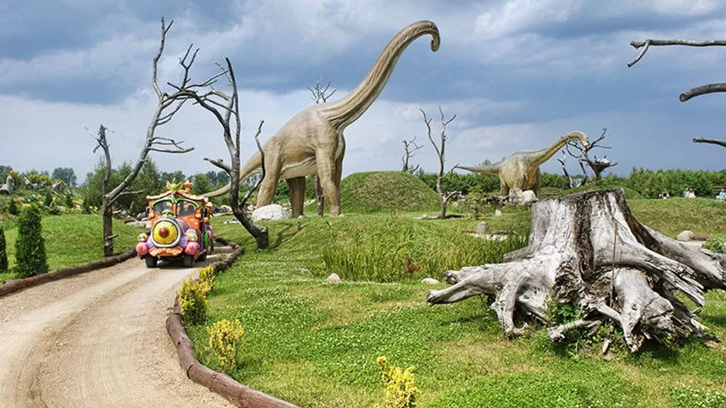 Dinosaurierpark in Łeba, Dinosaurierfiguren und ein Auto mit Touristen